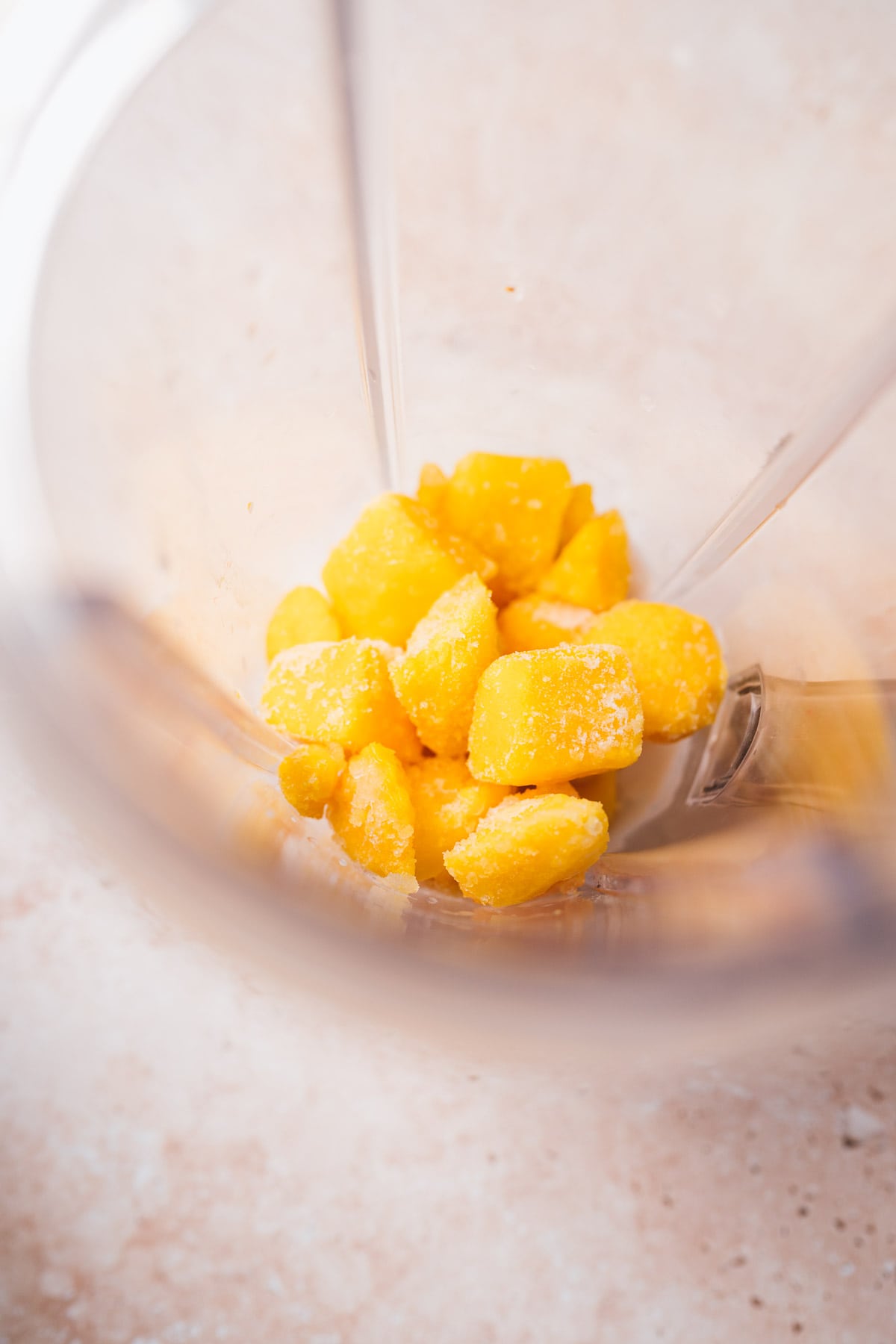 Top view of a blender container filled with frozen mango chunks.