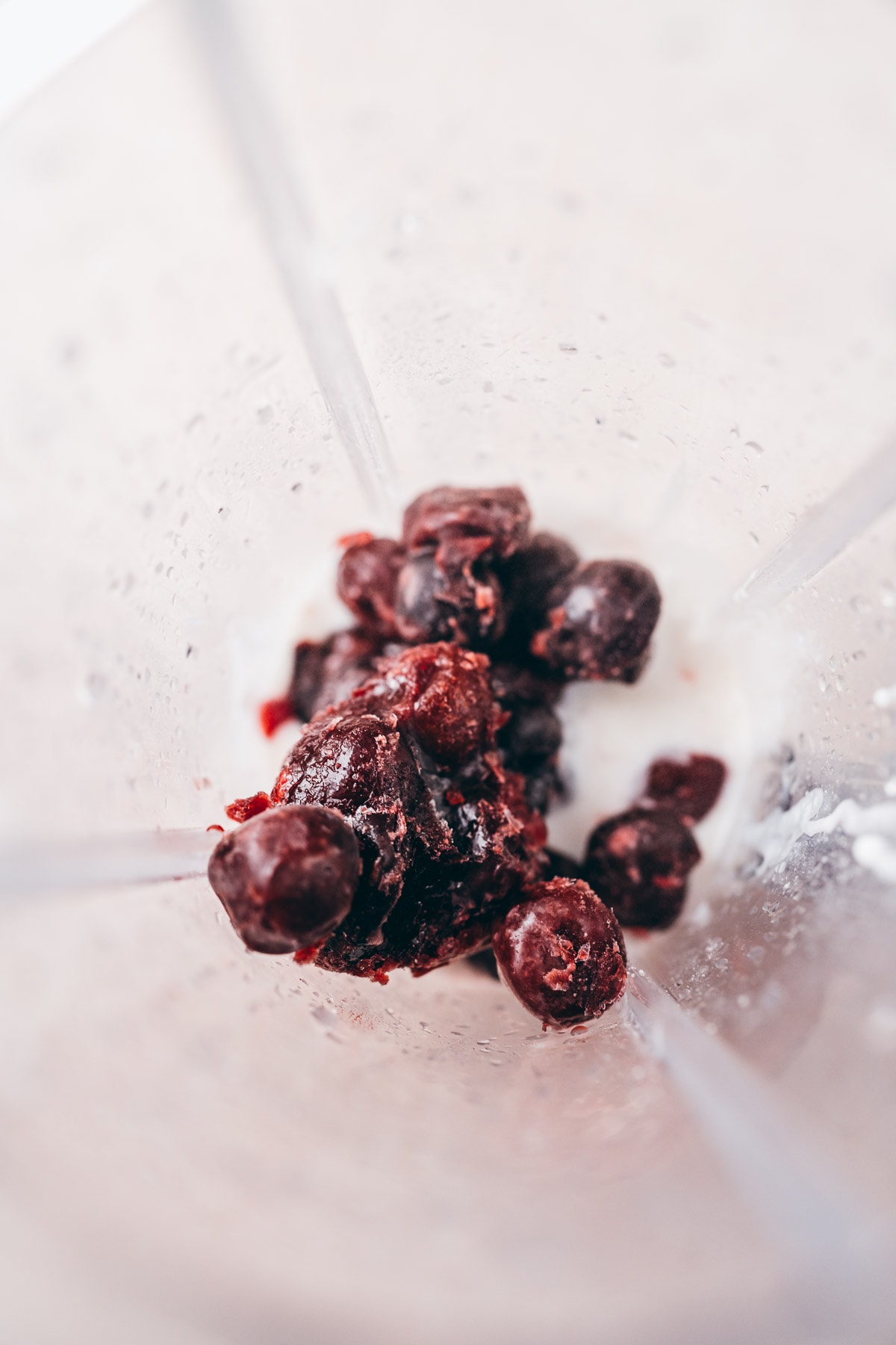 Top view of a blender container filled with frozen cherries.