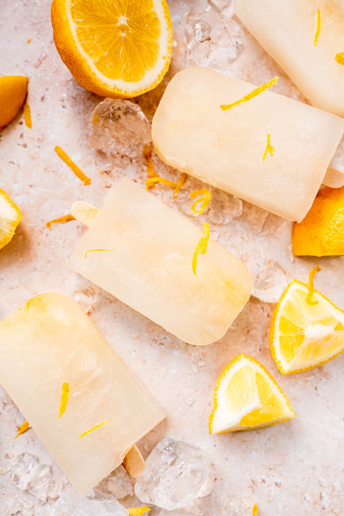 Homemade lemon ice pops resting on tan table garnished with fresh lemons.