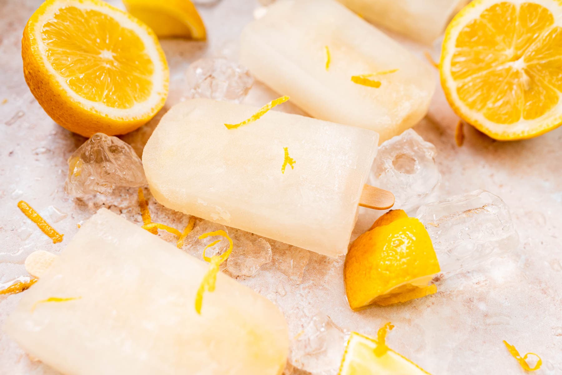 Homemade lemon popsicles resting on a tan table filled with ice and lemon slices.