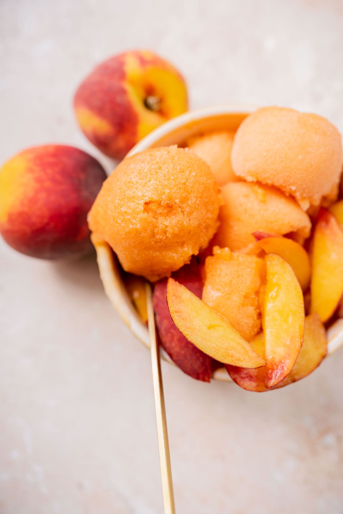 Close shot of a spoonful of peach sorbet resting in a small tan bowl.