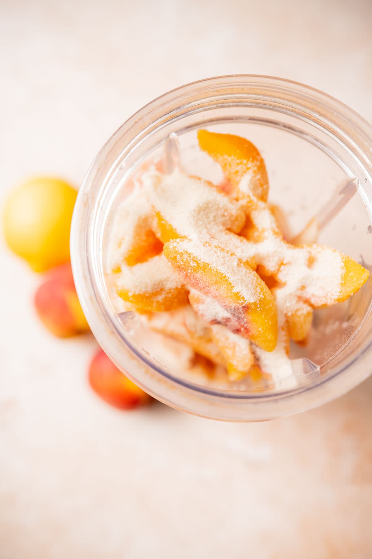 Top view of a blender container filled with peaches and sugar.