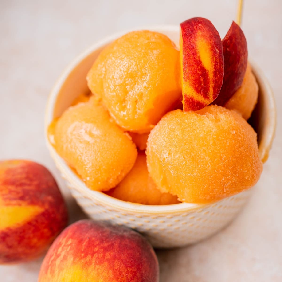 Close shot of a tan ceramic bowl filled with scoops of fresh peach sorbet garnished with peach slices.