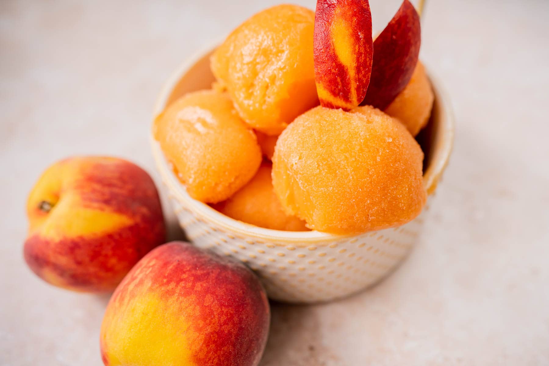 Close view of homemade peach sorbet in a small tan bowl garnished with fresh peaches.