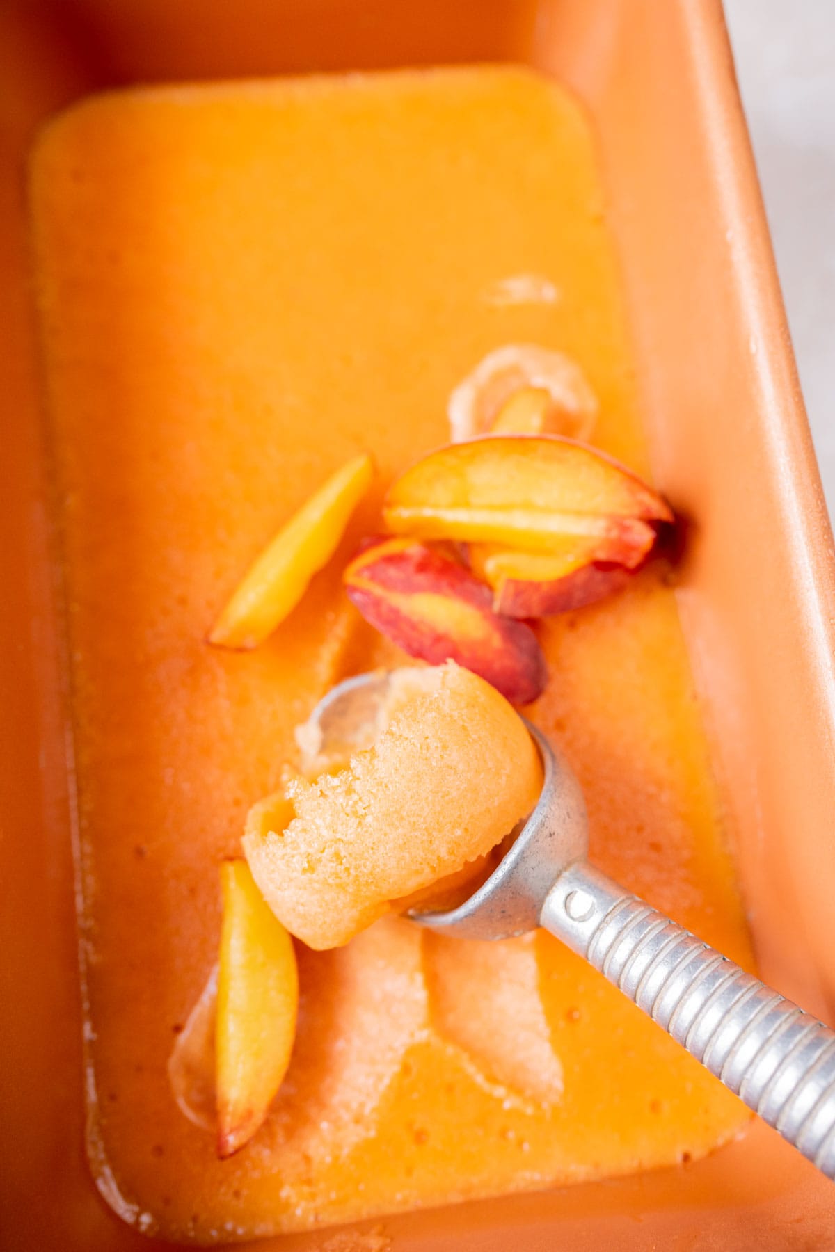 An ice cream scoop resting in a loaf pan of homemade peach sorbet.