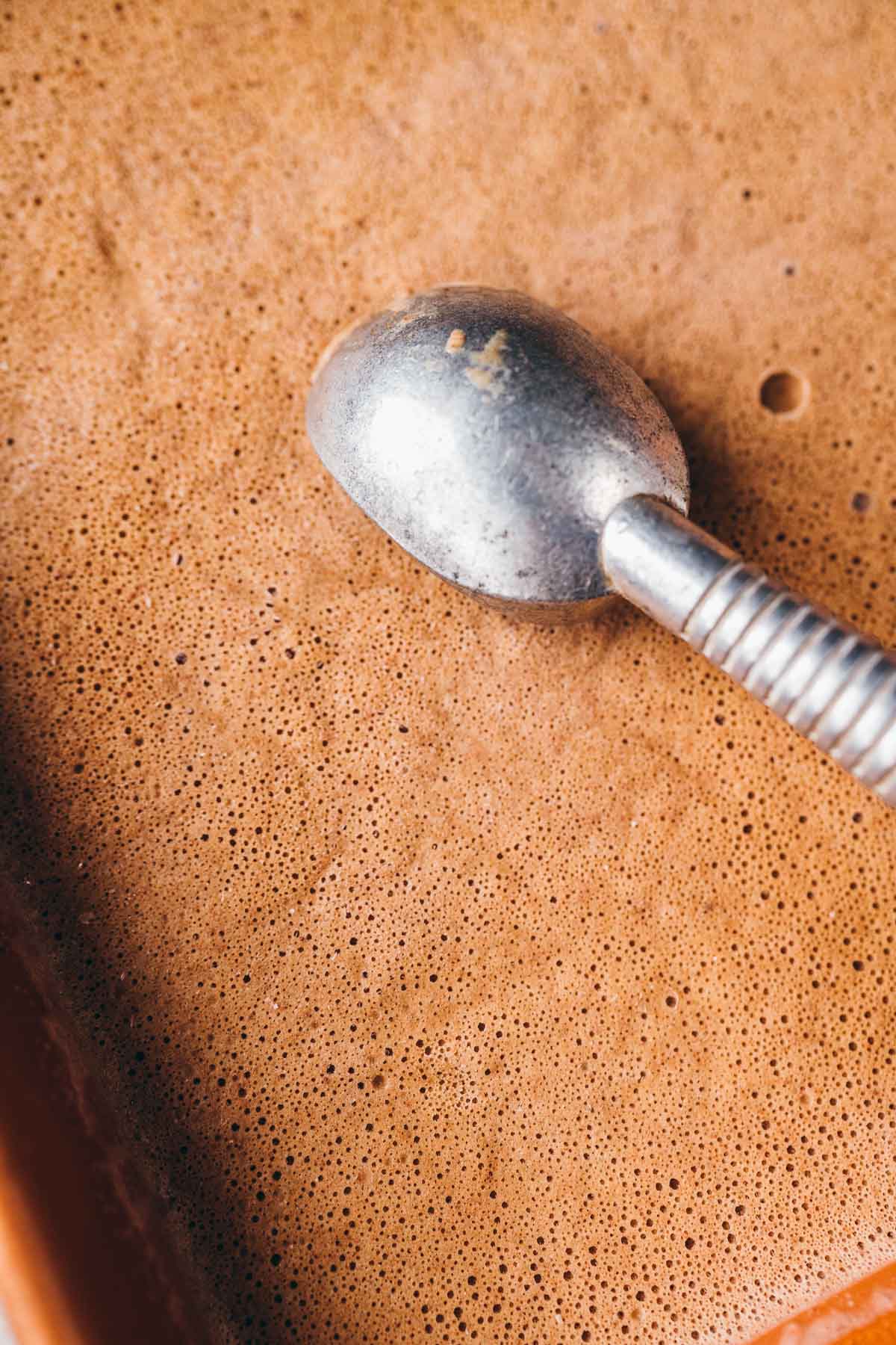 A silver ice cream scoop resting in a pan of homemade coffee ice cream.