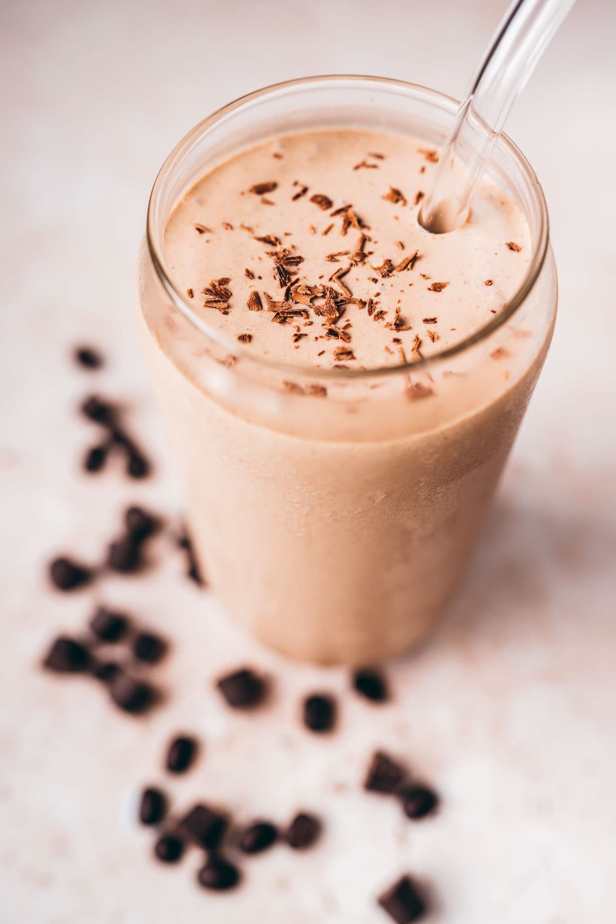 A tall clear glass filled with a homemade coffee milk shake garnished with grated chocolate.