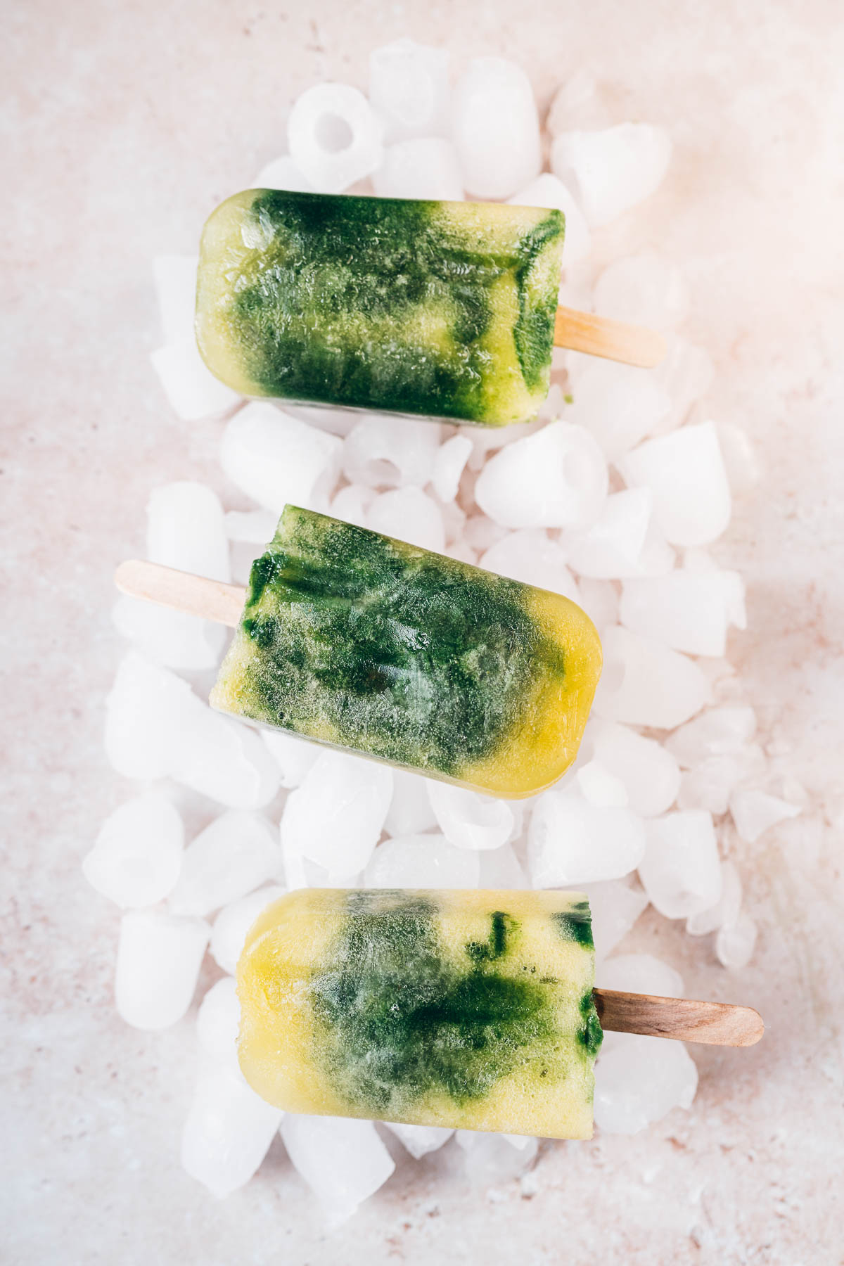 Three homemade ice pops resting on a table covered in ice.