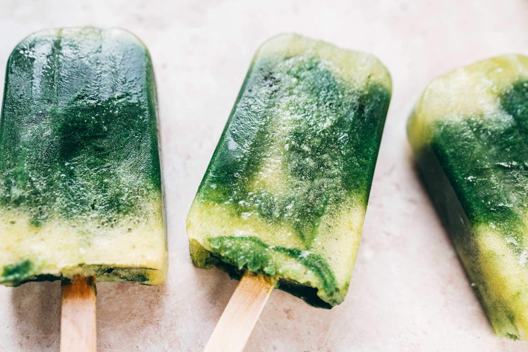 Three homemade ice pops rest on a tan table.