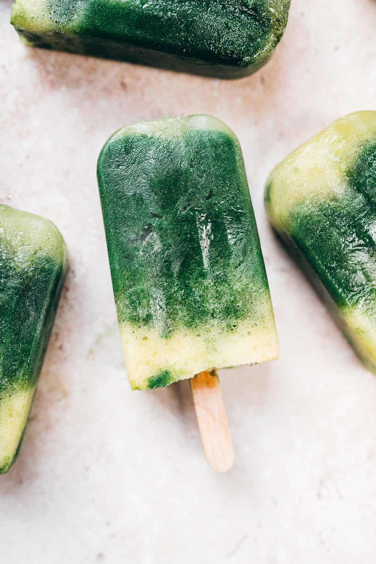 Homemade green and yellow ice pops rest on a tan table.