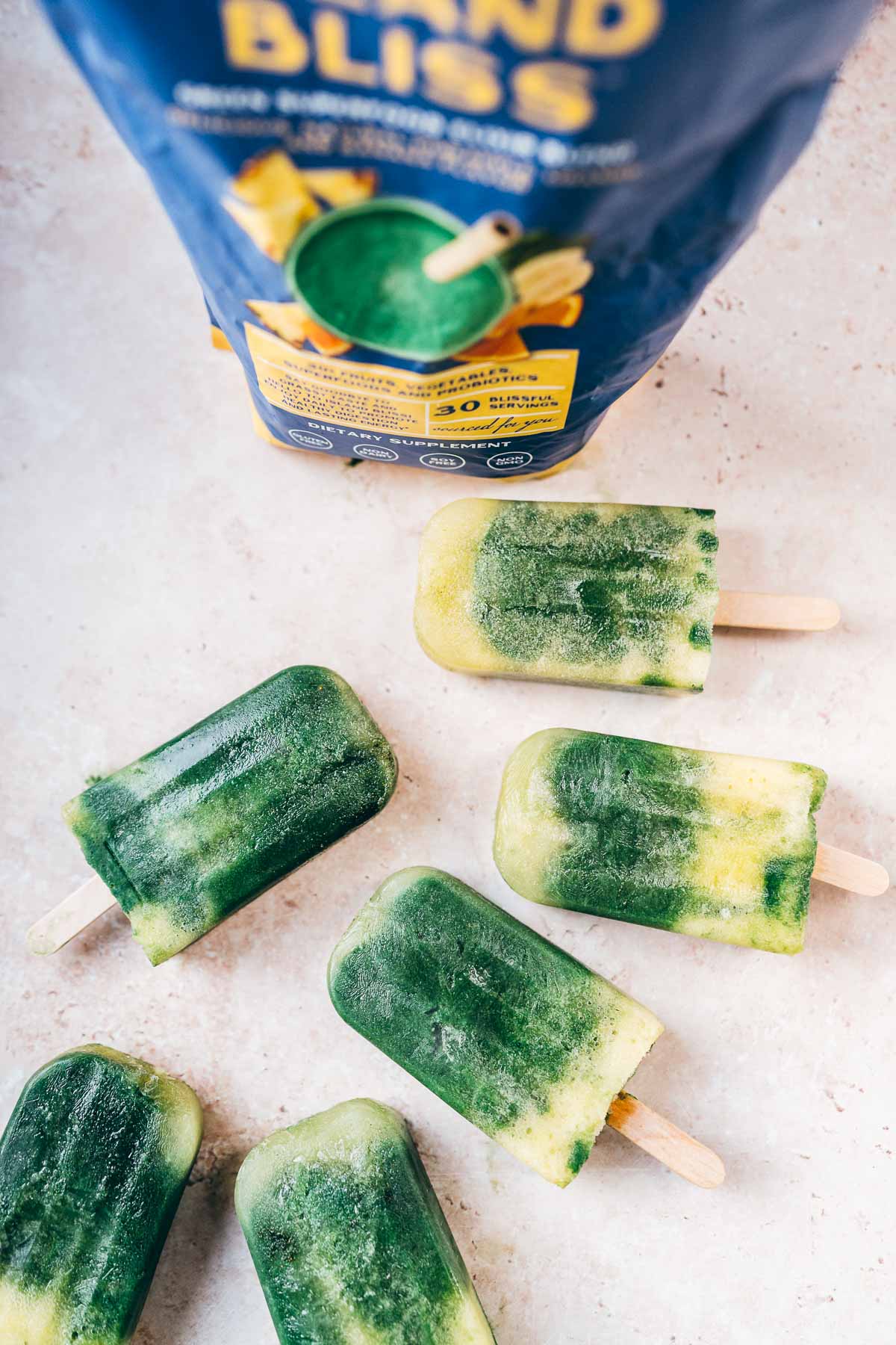Green and yellow ice pops rest on a tan tabletop.