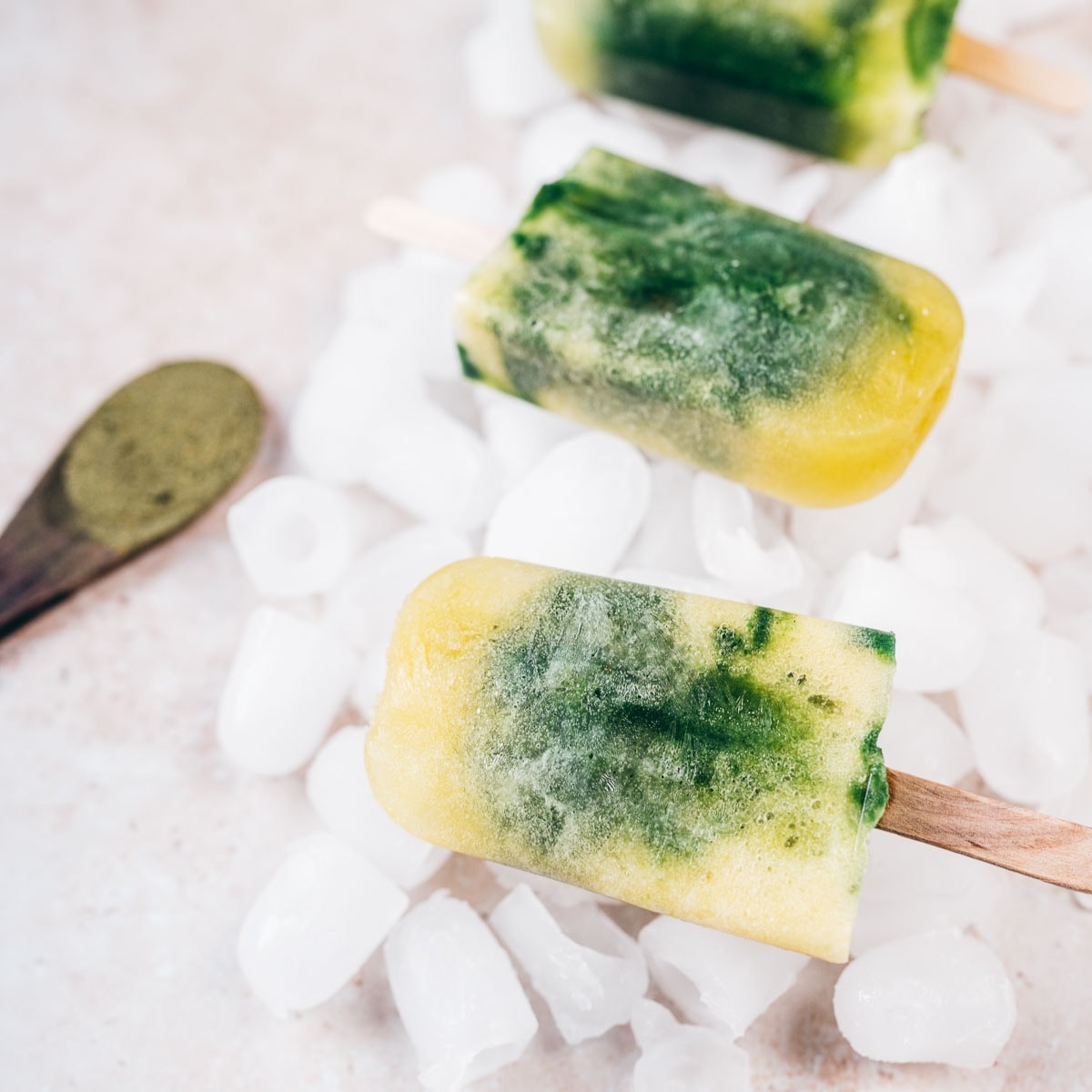 Homemade green and yellow popsicles resting on ice cubes.