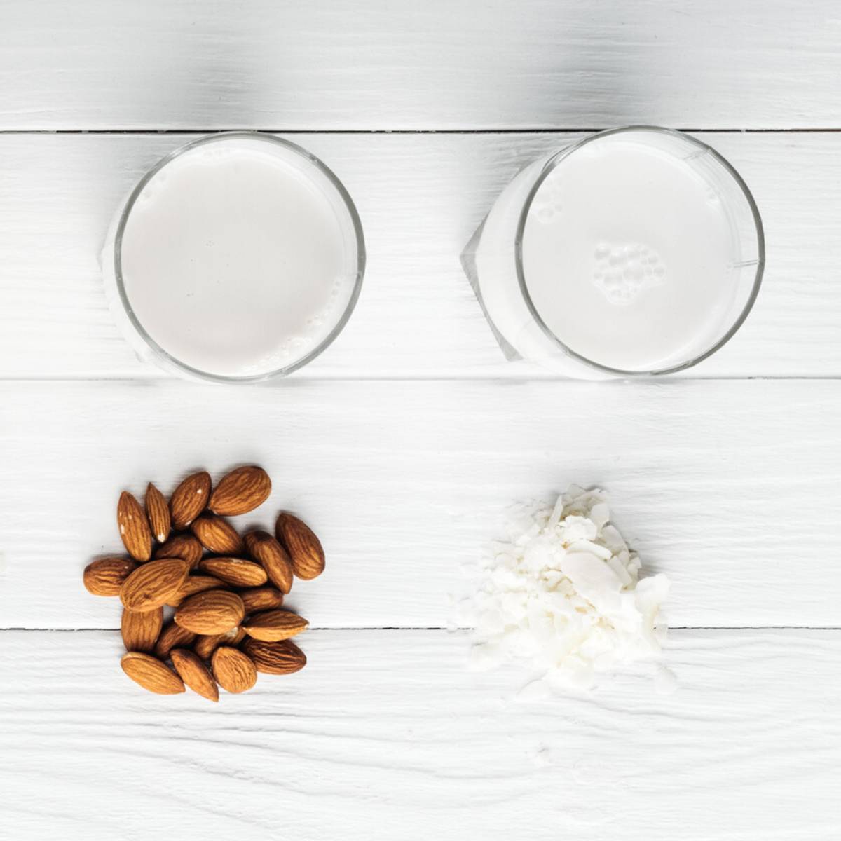 Two clear glasses, one with coconut milk, one with almond milk.