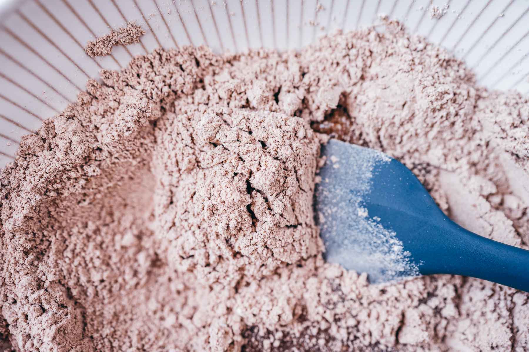 A ceramic bowl with dry cookie ingredients and a blue spatula.