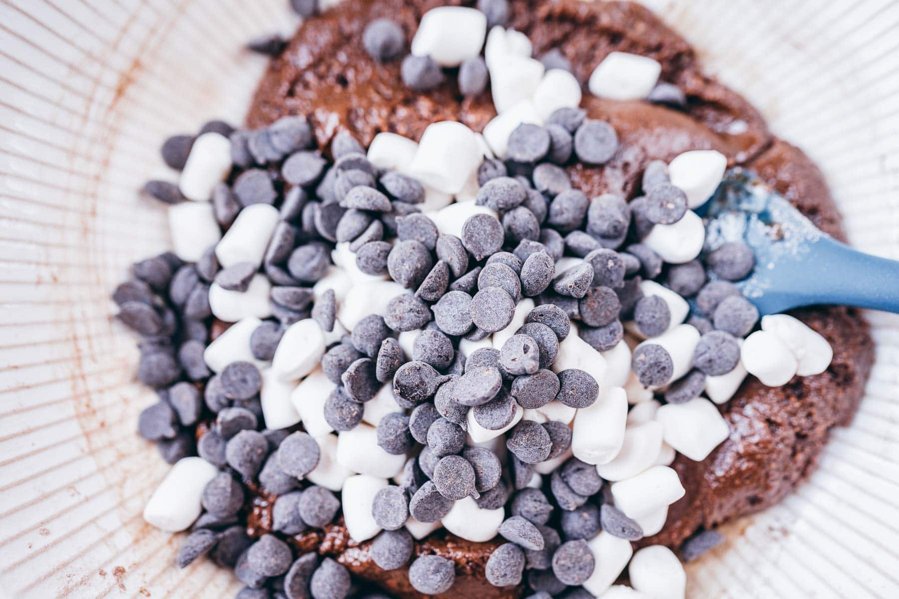 A brown cookie batter topped with mini marshmallows and dark chocolate chips.