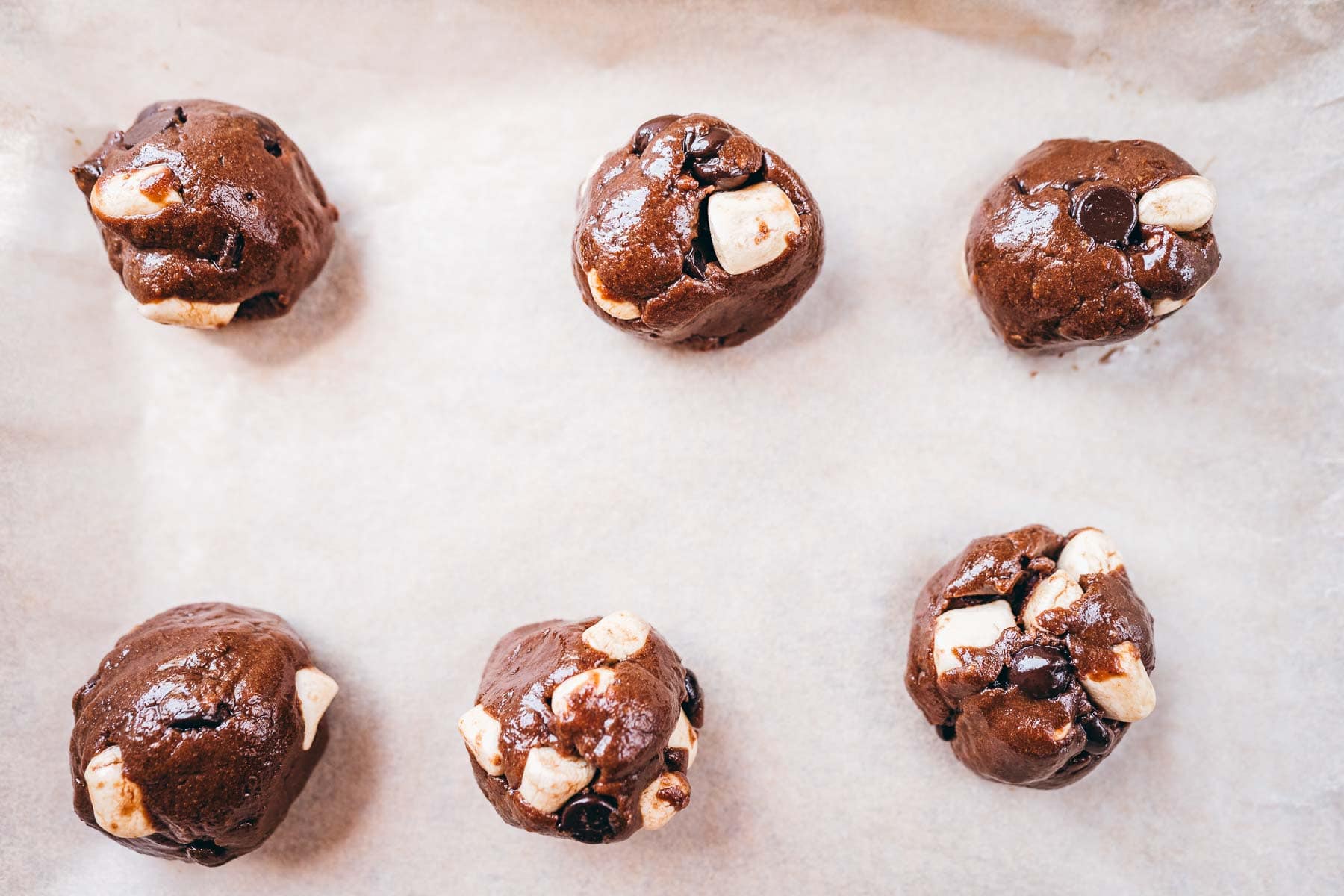 Rounds of uncooked cookie batter on parchment paper.
