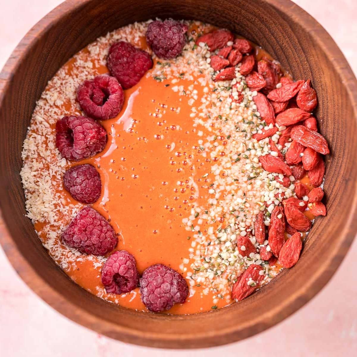A close shot of a wooden bowl filled with a light red smoothie.