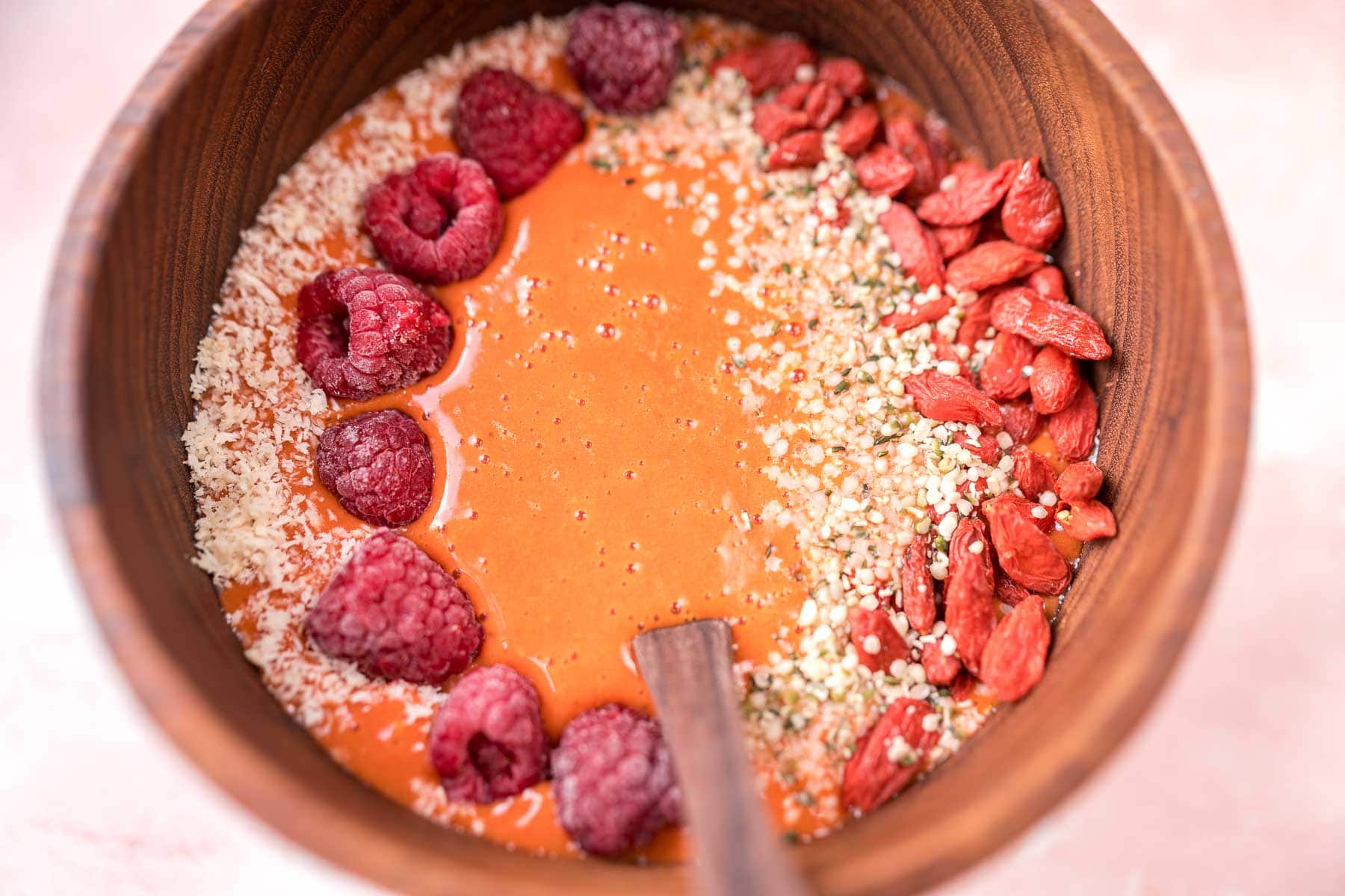 A close shot of a wooden bowl filled with a light red smoothie.
