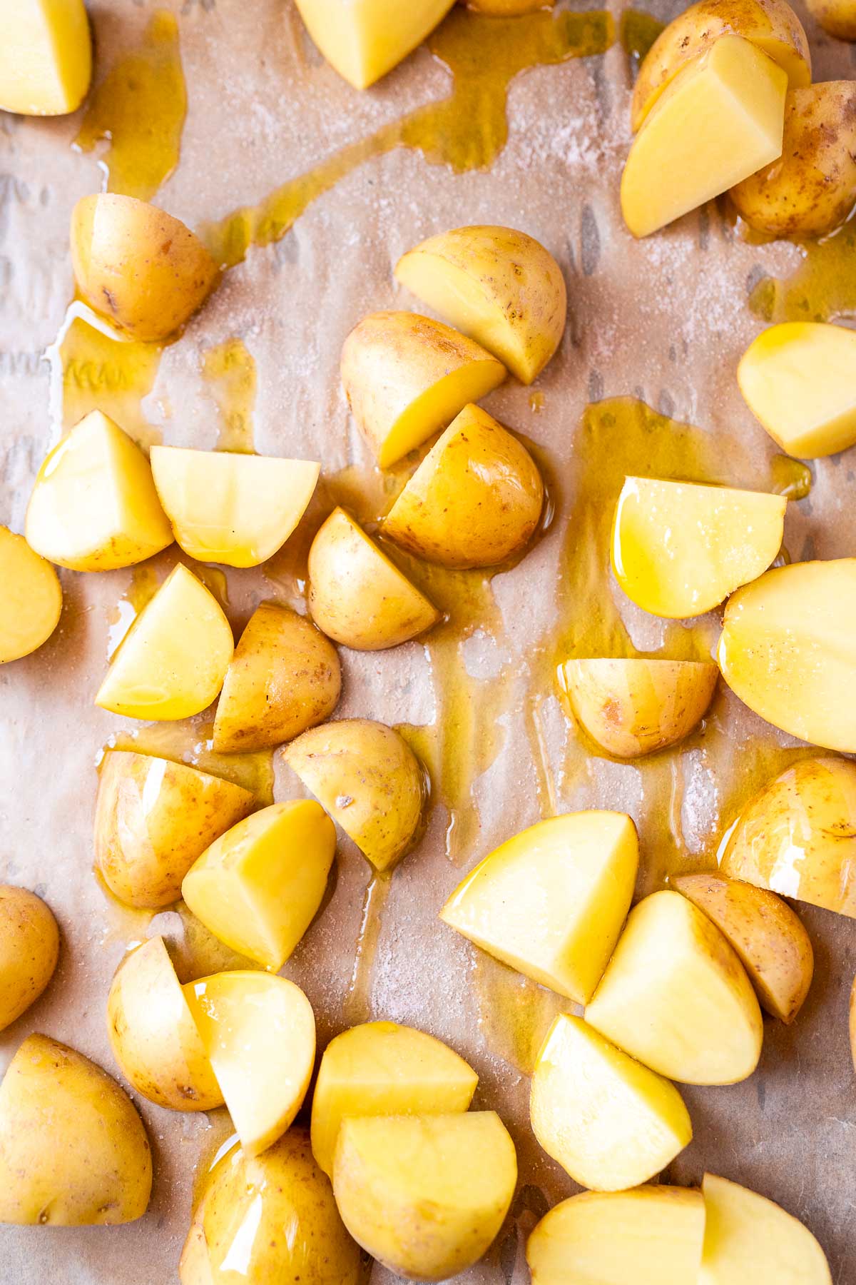 Quartered yellow potatoes drizzled with oil on a parchment lined baking sheet.