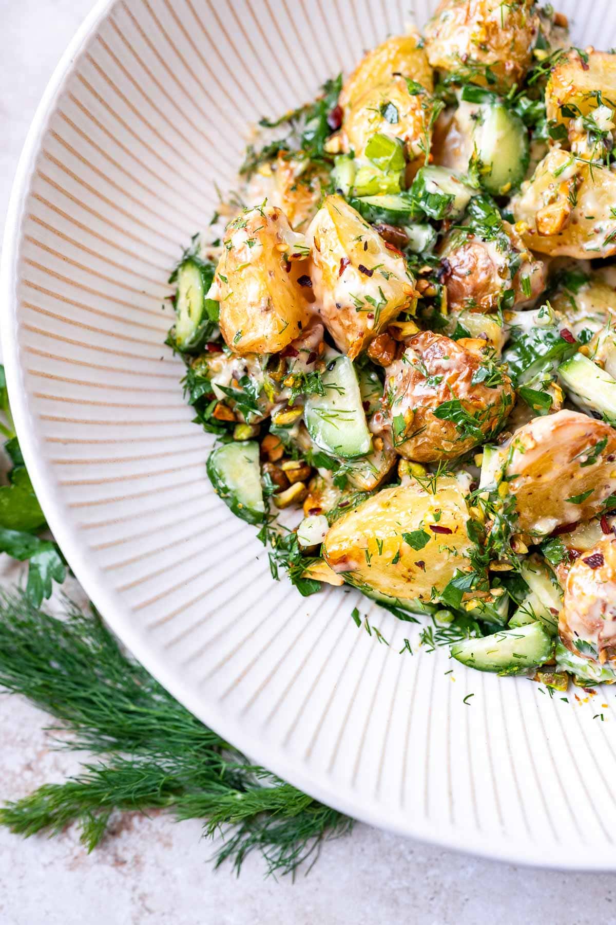 Roasted potato salad with fresh green herbs resting in a large white ceramic salad bowl.