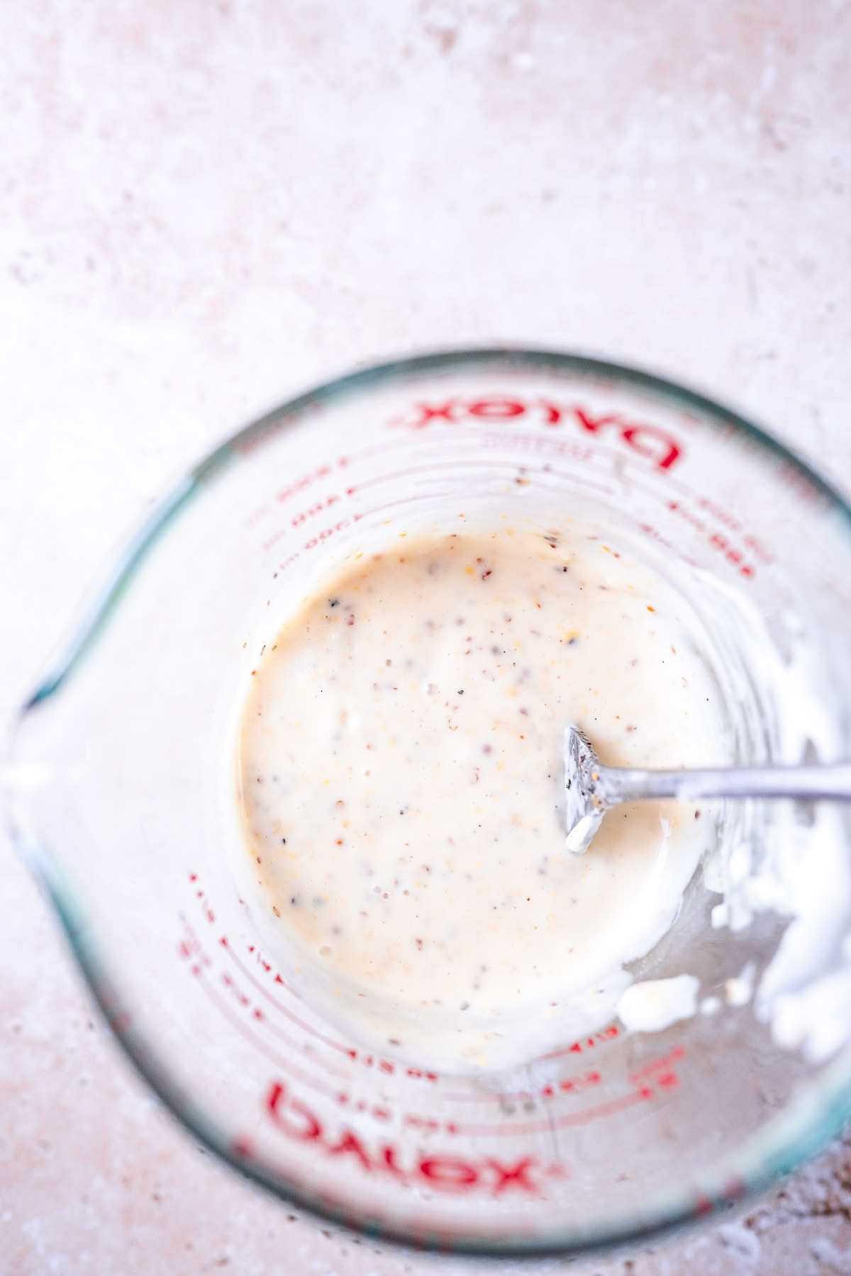 A measuring cup filled with a creamy white homemade dressing.