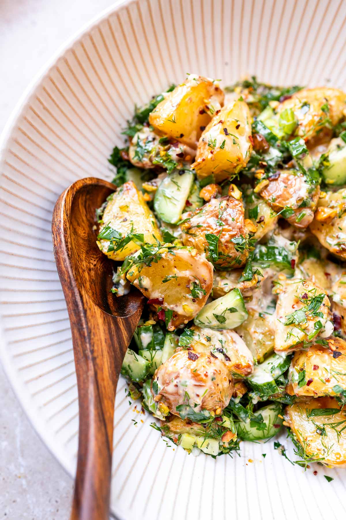 Close shot of herbed potato salad in a large white ceramic bowl with a large wooden spoon.