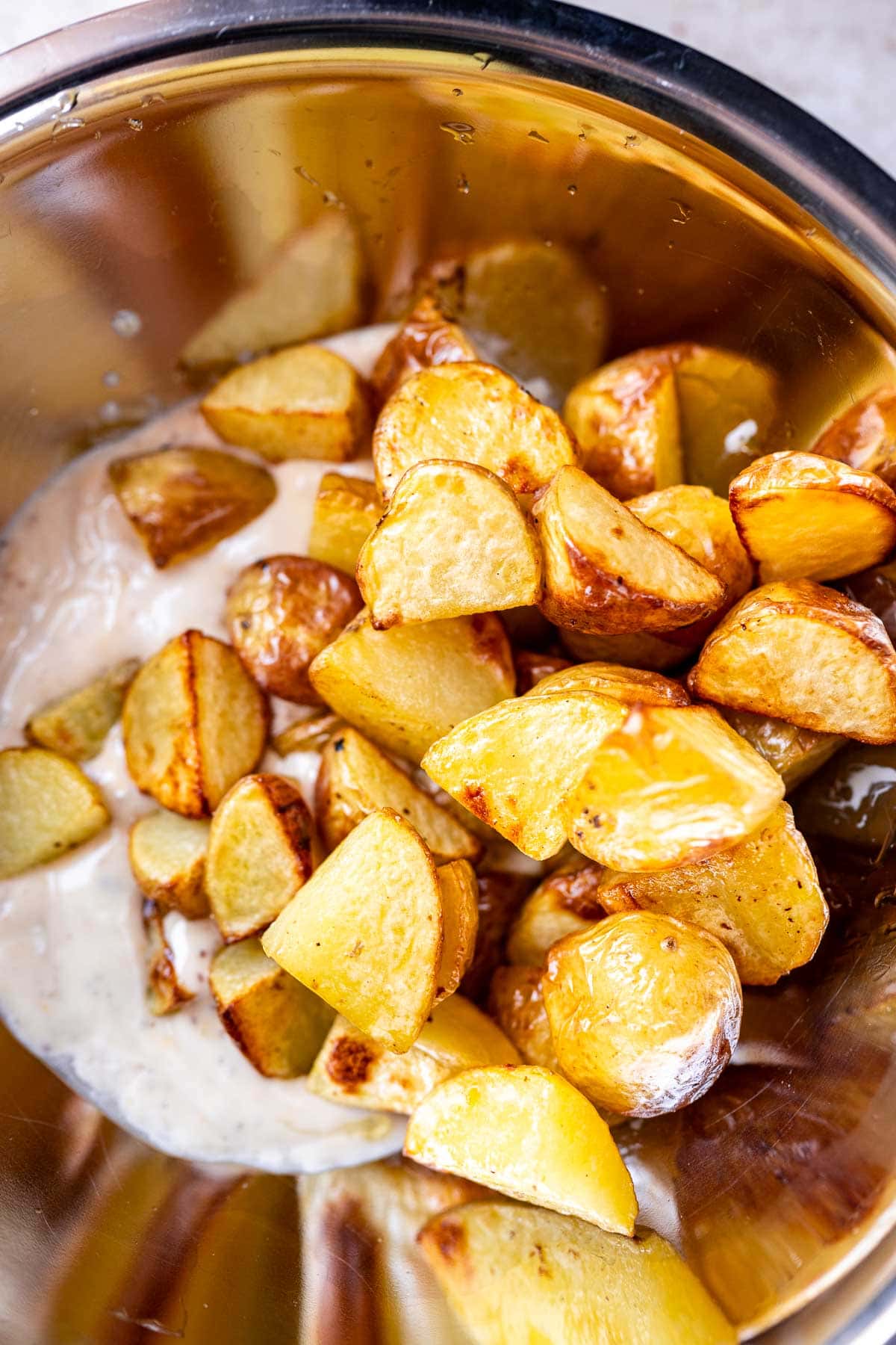 Freshly roasted potatoes being tossed in a mixing bowl with a white dressing.