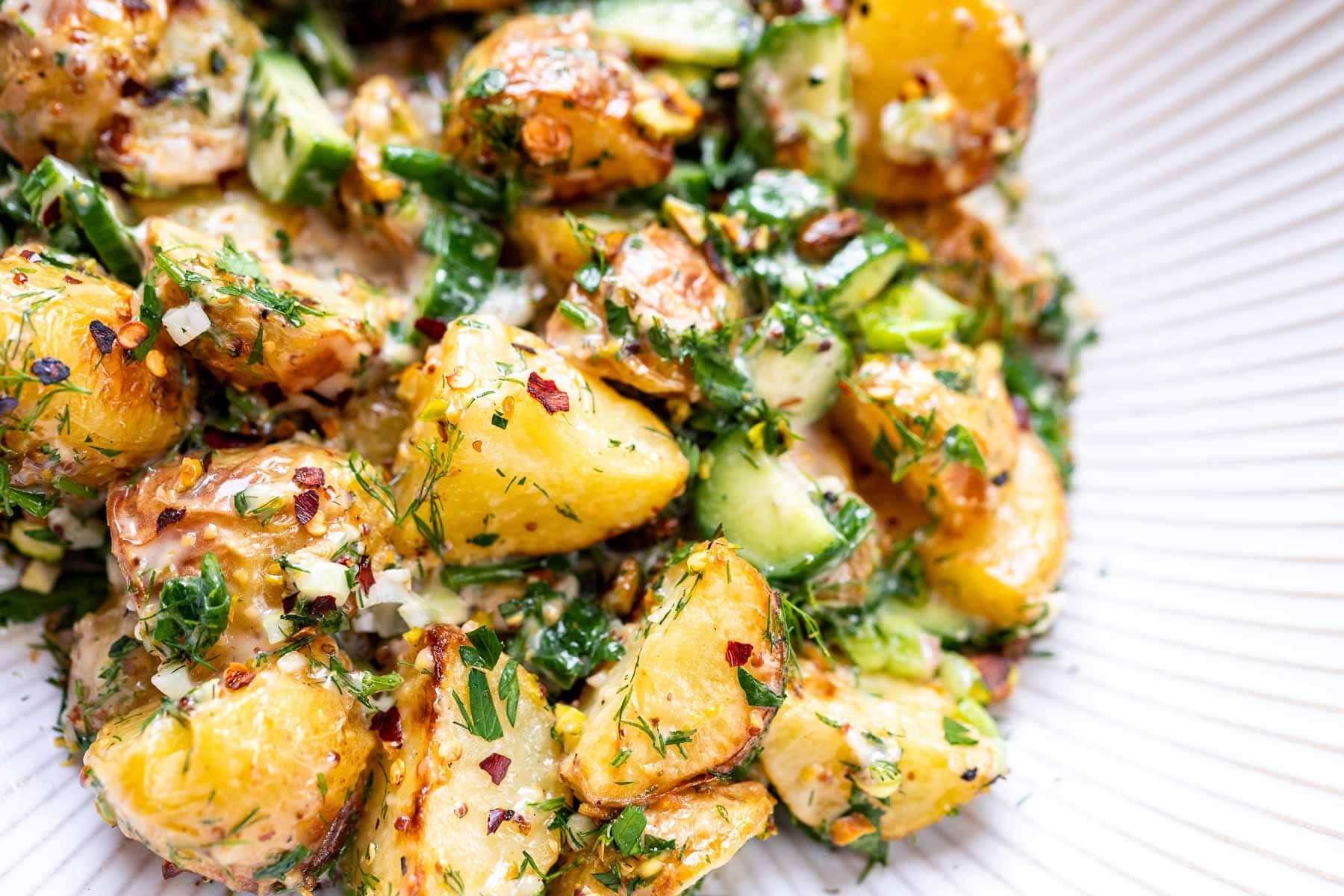 A close shot of a roasted potato salad in a white ceramic bowl.