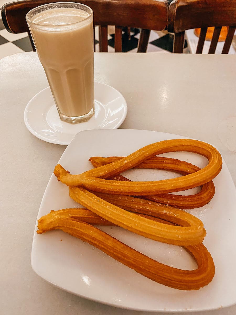 Churros on a white plate next to a glass of Spanish horchata.