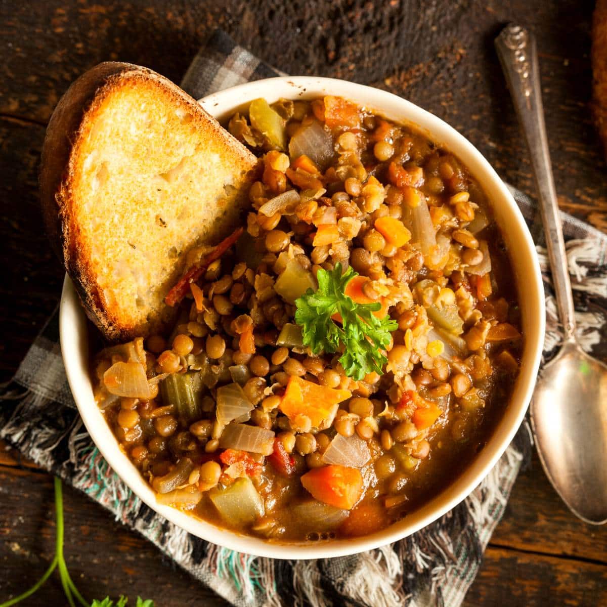 A white dish filled with lentil stew and crusty bread.