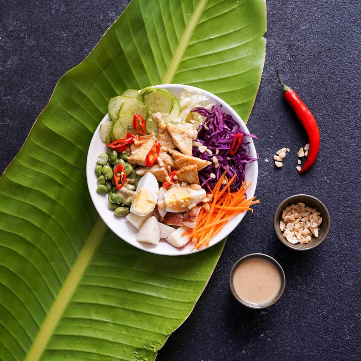 Indonesian gado gado resting on a large green leaf on a dark table.