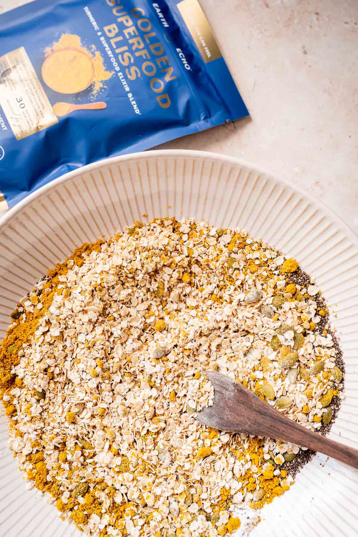 A golden milk-infused bowl of granola topped with fruits and served with a wooden spoon.