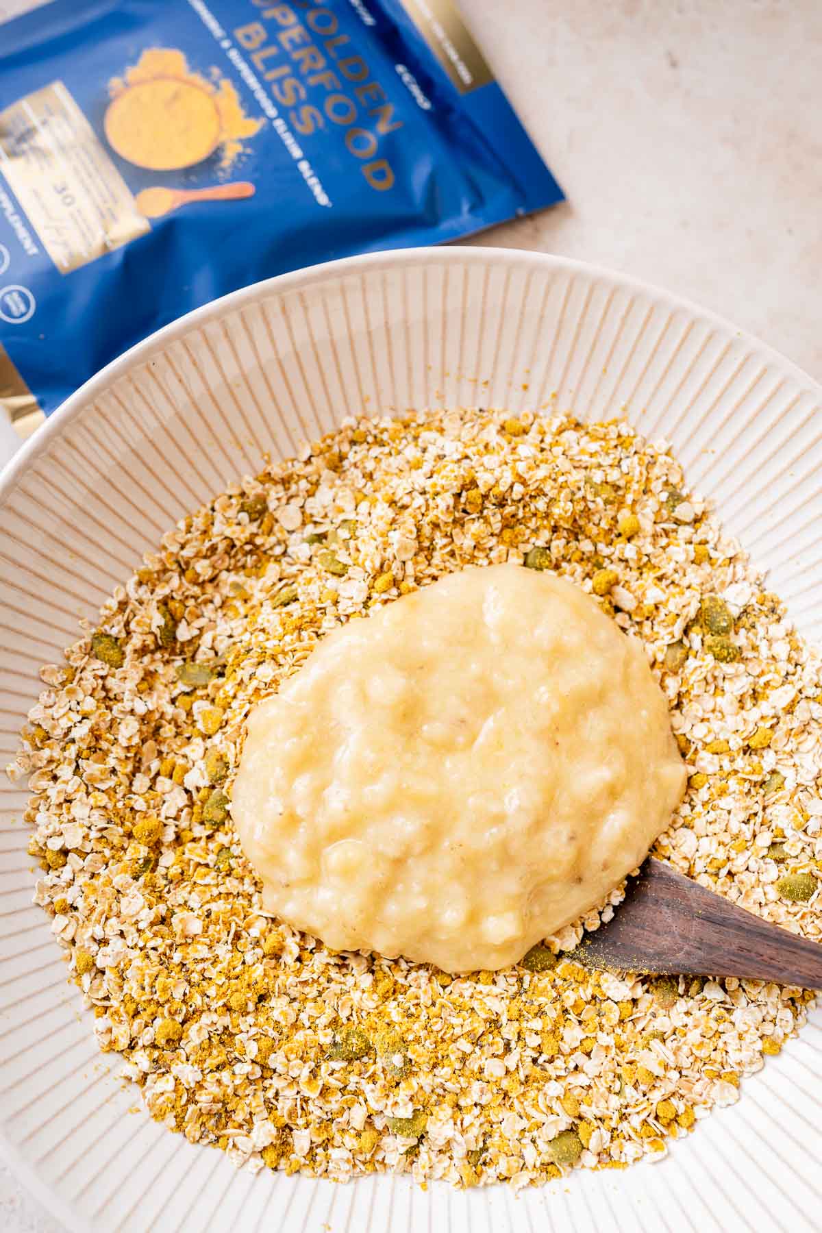 A bowl of golden granola on a table next to a bag of granola.