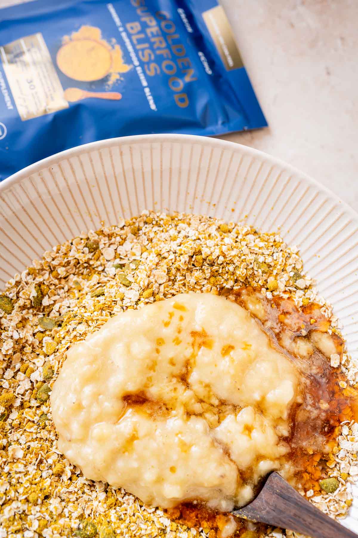 A bowl of golden oats with a spoon next to a bag of oats.