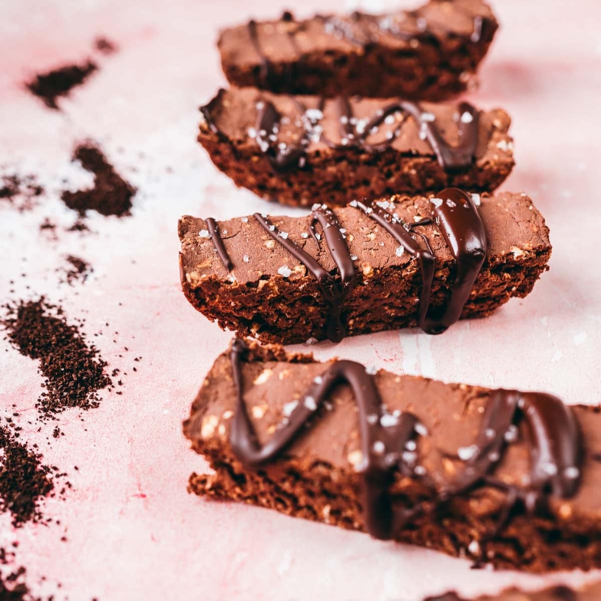 Four chocolate protein bars resting on a pink table scattered with ground coffee.