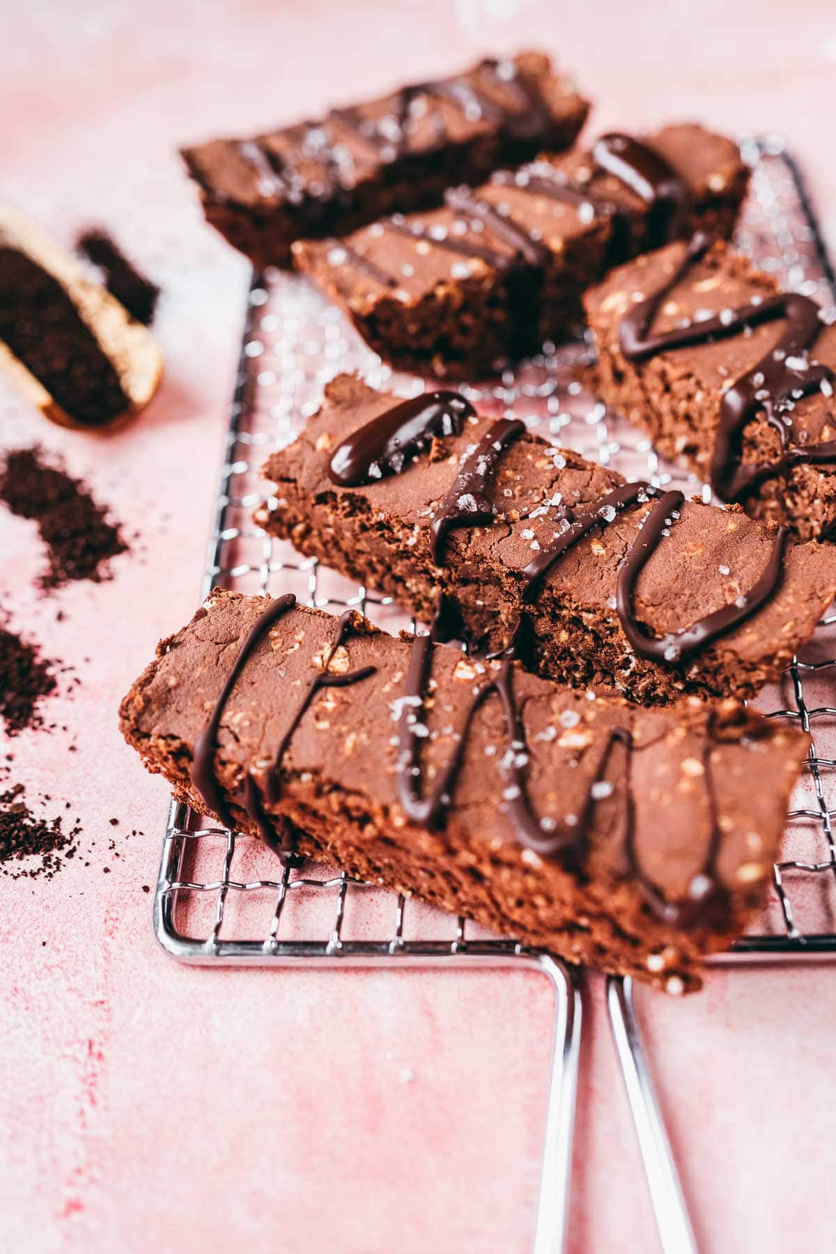 Chocolate protein bars resting on a silver cooling rack on a pink table.