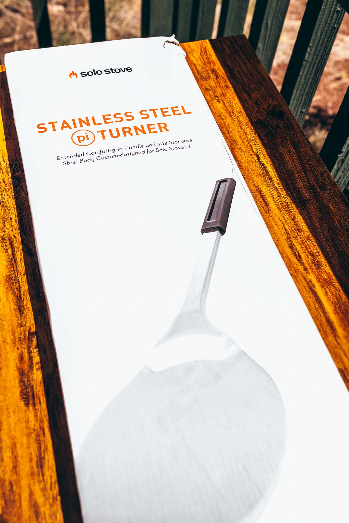 A stainless steel spatula on a wooden table in the presence of a solo stove pizza oven.