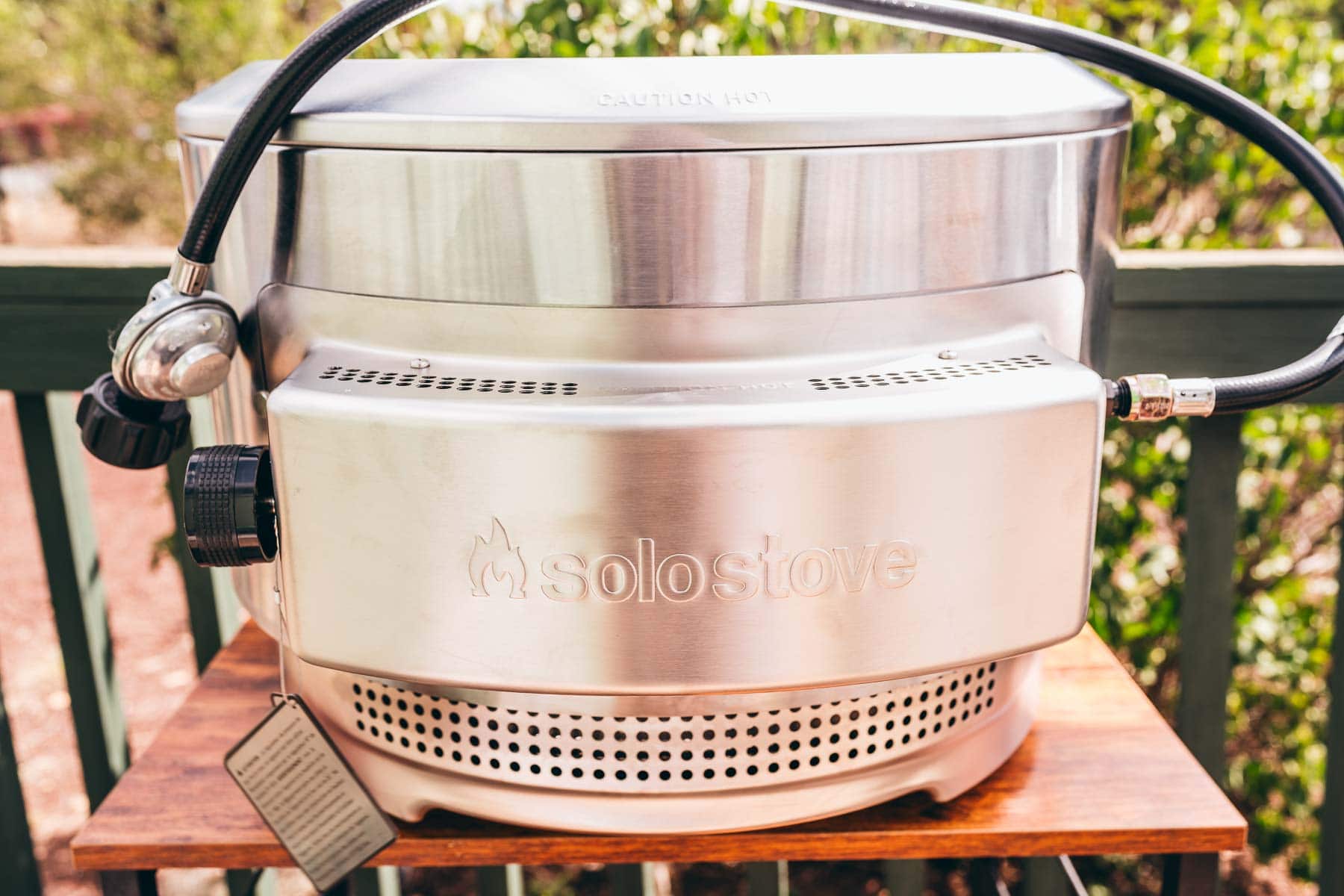 A stainless steel water jug sitting on a wooden table, next to a Solo Stove pizza oven.