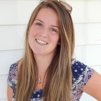 A young woman smiling in front of a white house.