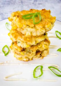 A stack of corn fritters on a white plate.