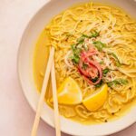 A bowl of golden noodle soup with lemon slices.