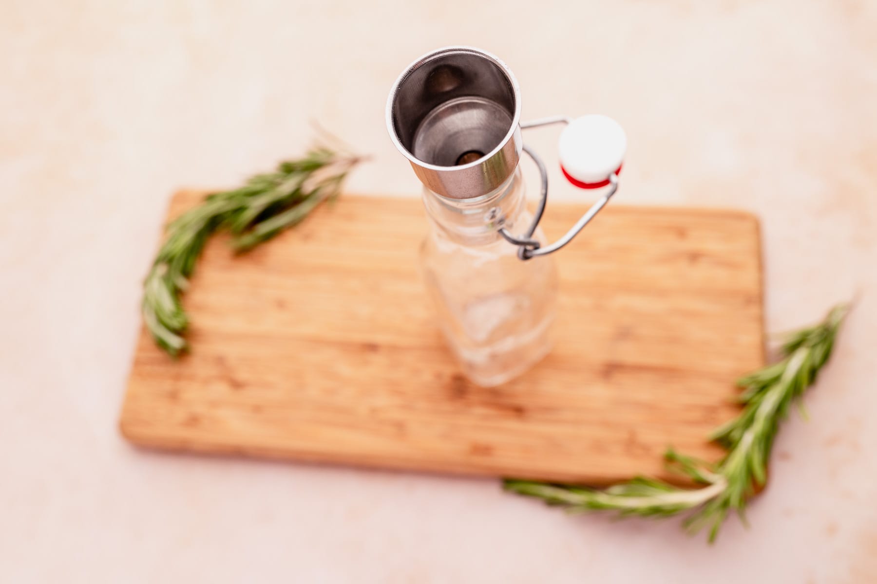 A bottle of olive oil with rosemary sprigs on a wooden cutting board, infused with rosemary.