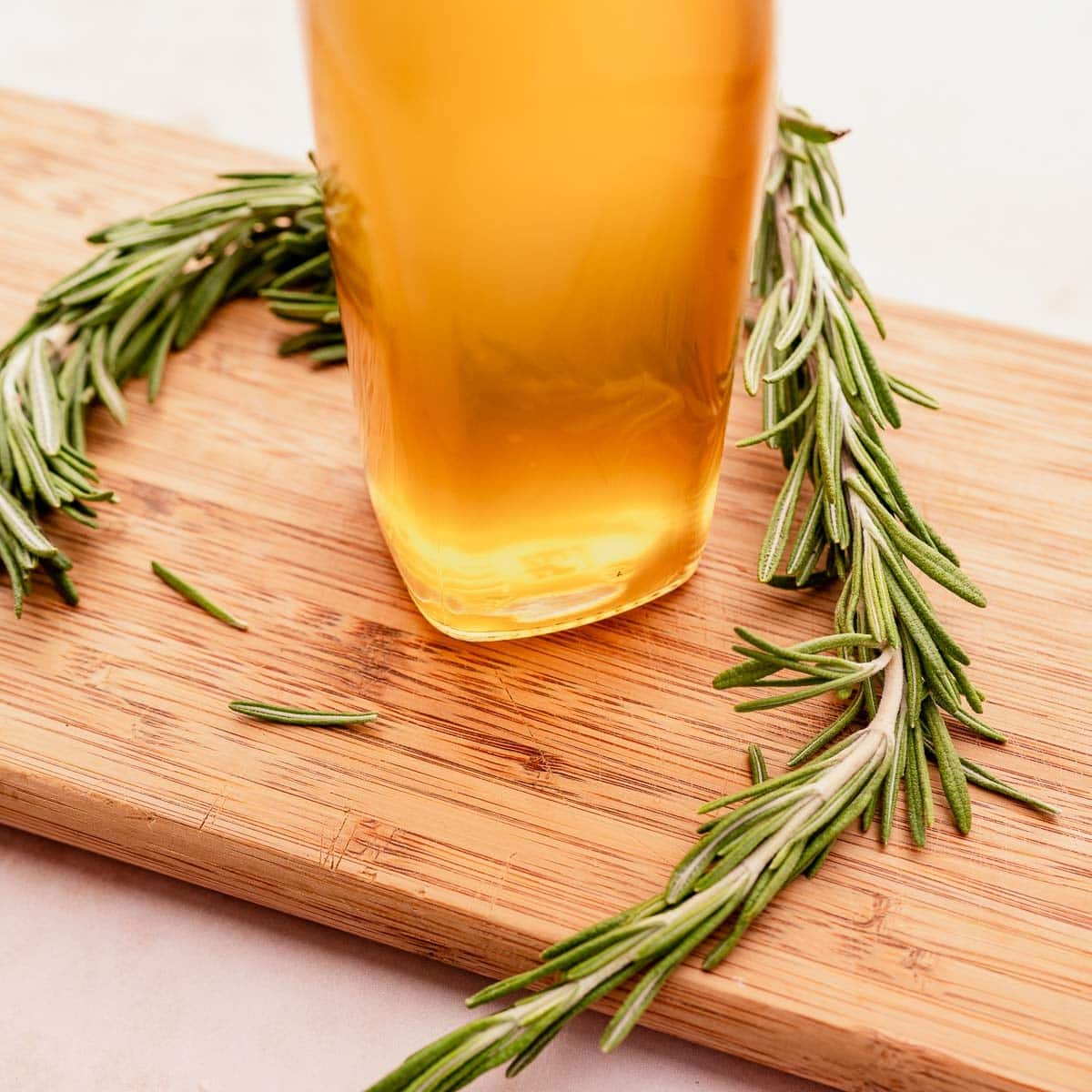 A glass of honey with rosemary sprigs on a cutting board, accompanied by a dollop of rosemary simple syrup.