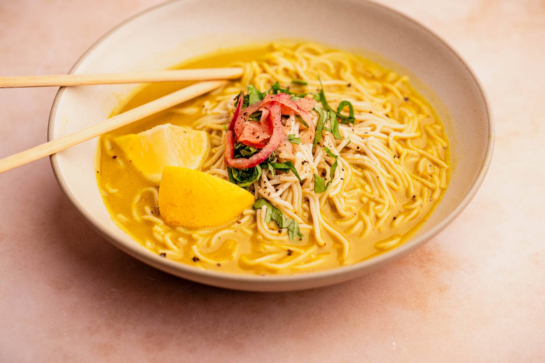 A bowl of golden noodle soup with chopsticks.
