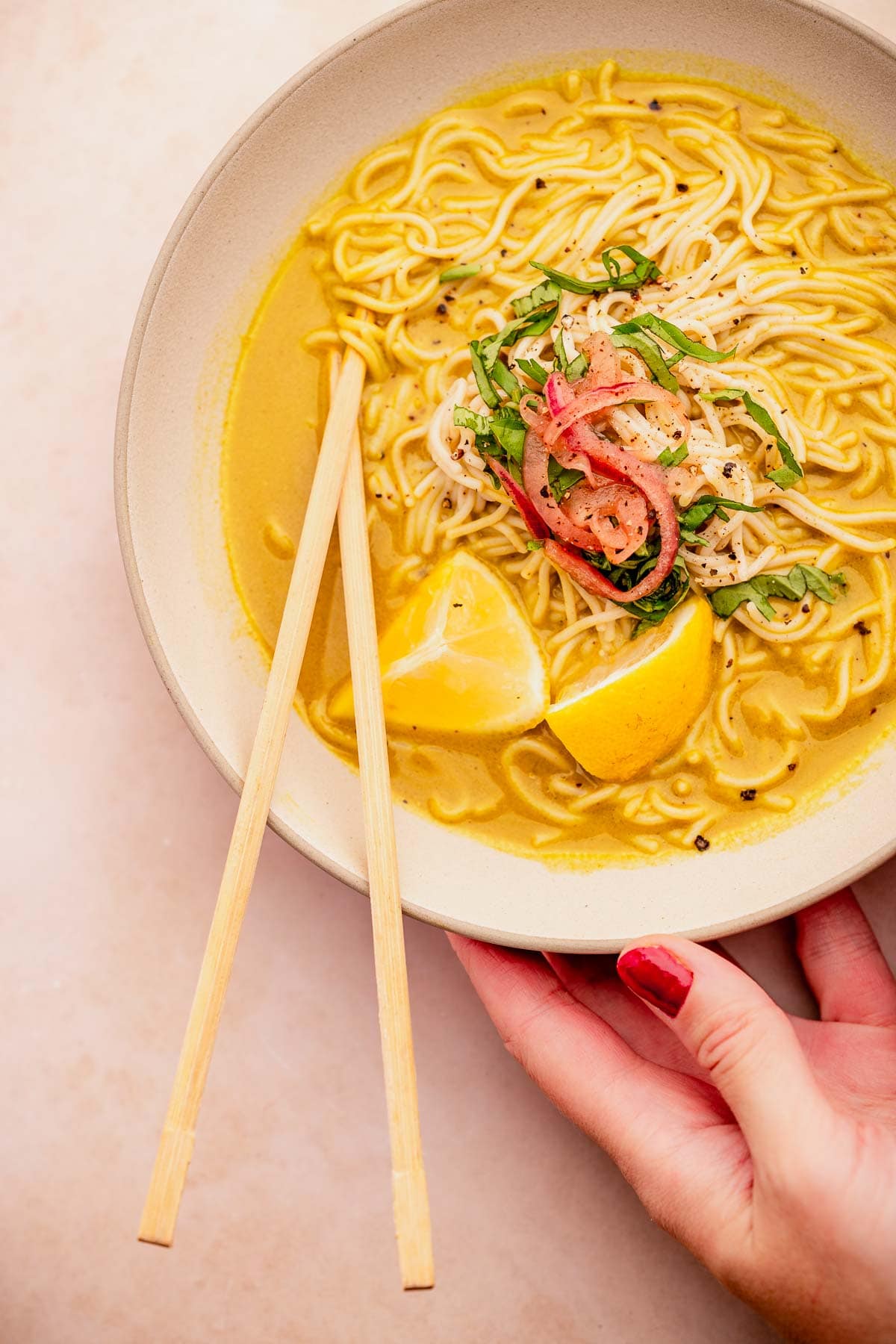 A person holding a bowl of golden noodles with chopsticks.