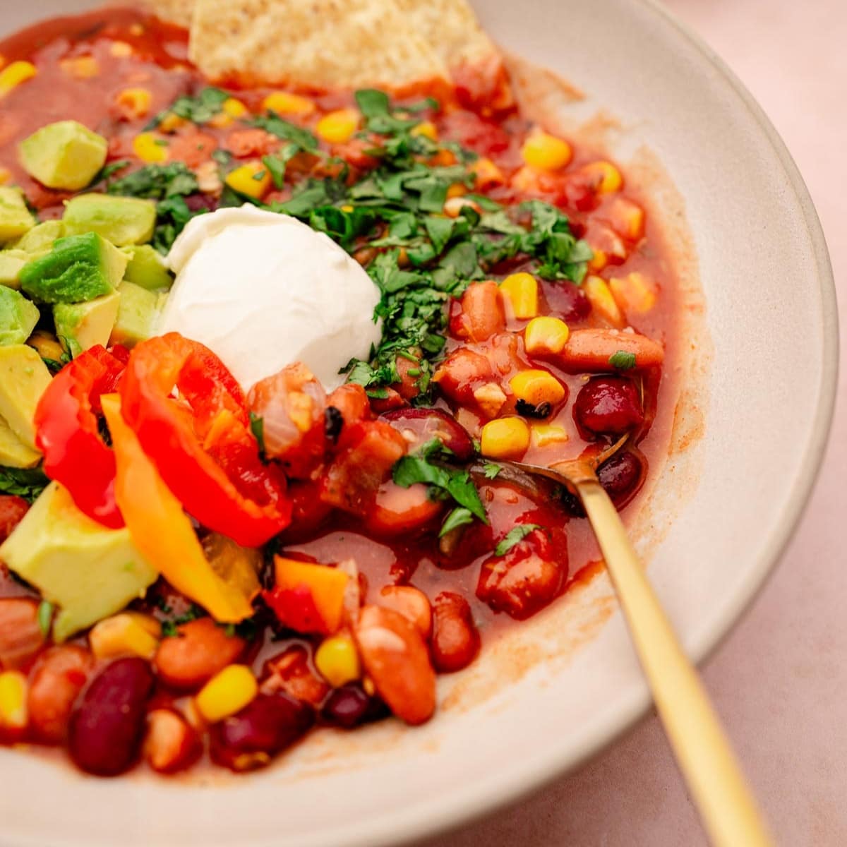 A tan ceramic bowl filled with a veggie chili topped with sour cream and fresh green  cilantro.