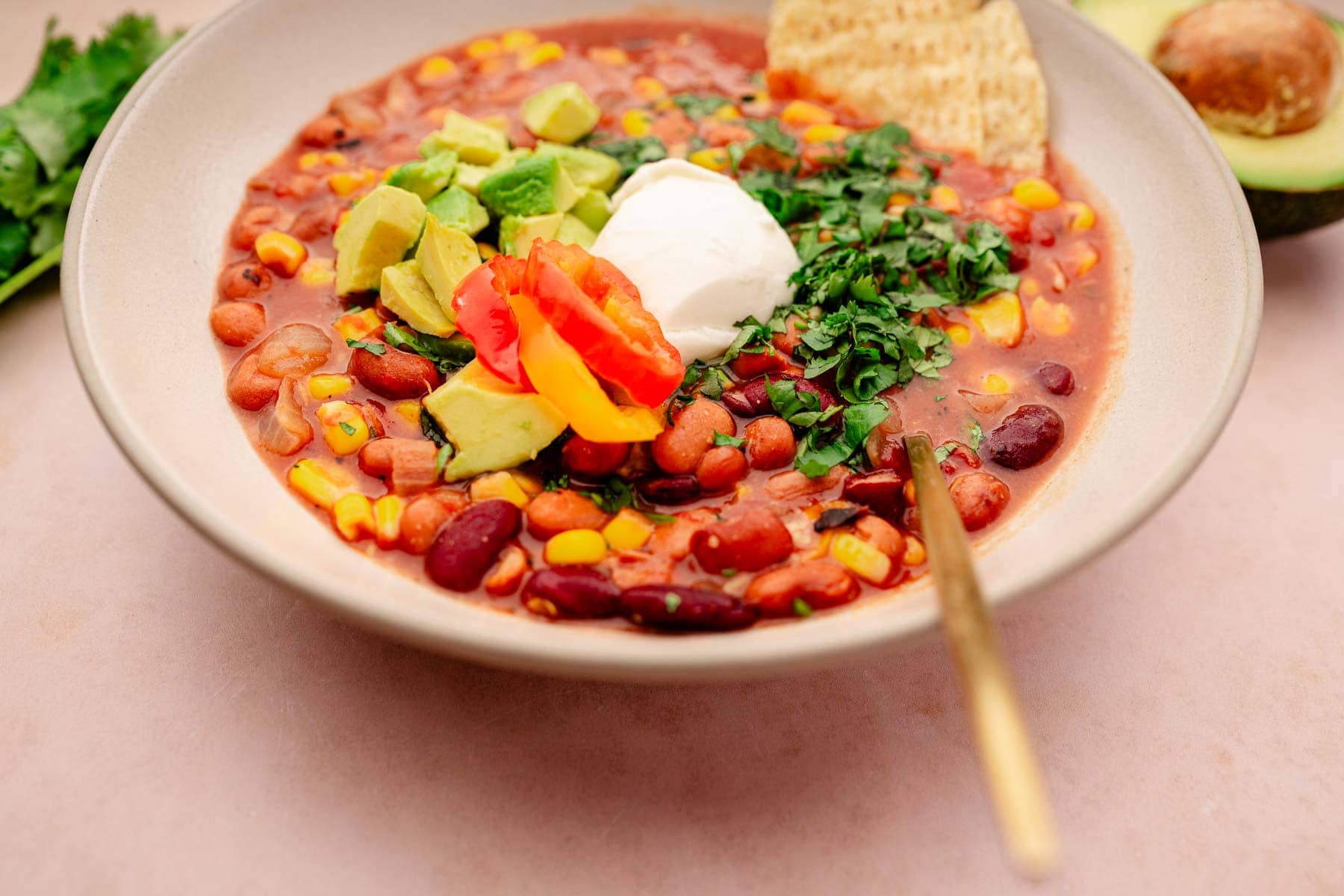 A slow cooker vegetarian chili packed with beans, corn, avocado, and topped with a dollop of sour cream.