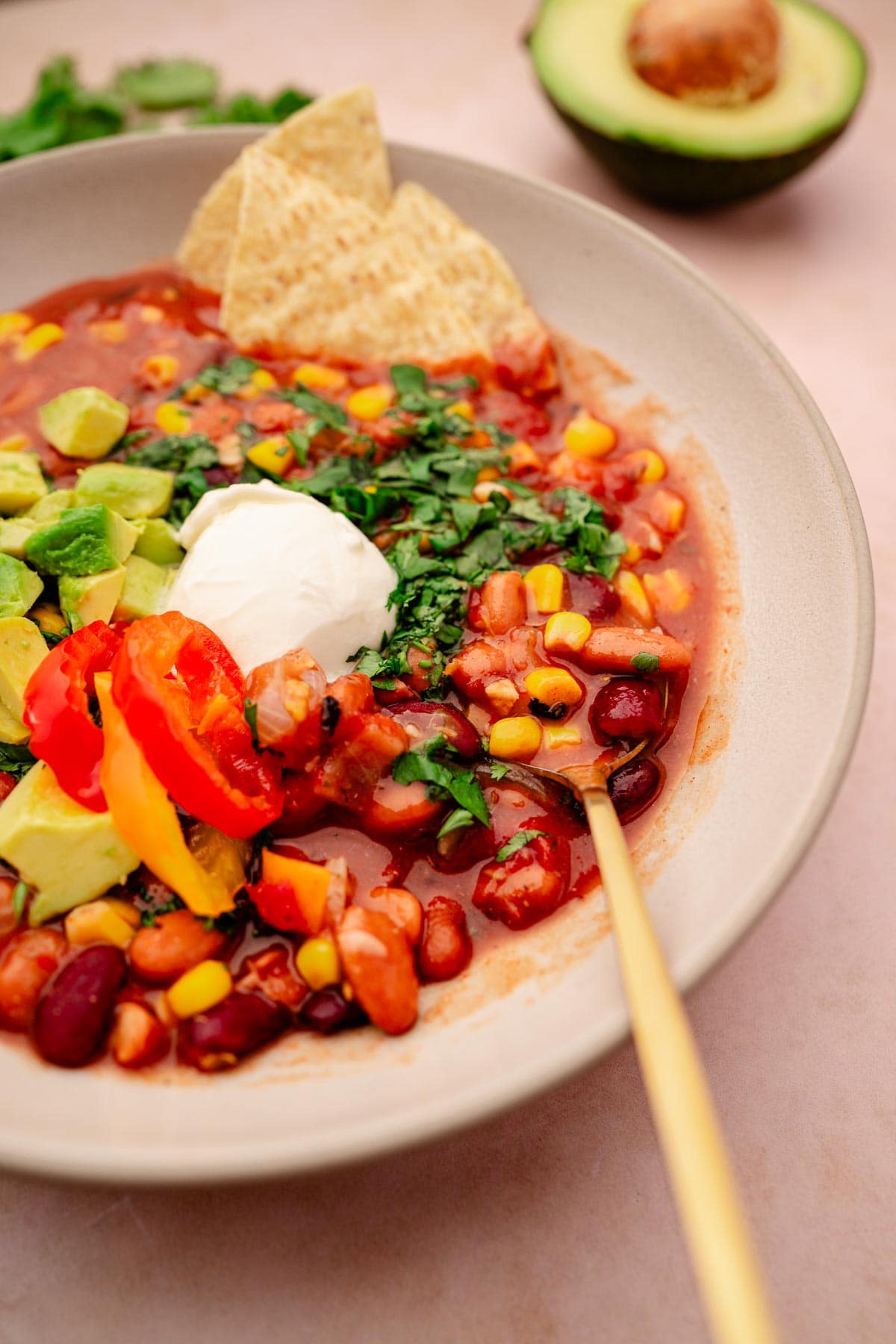 A slow cooker vegetarian chili with bean and vegetable soup, topped with avocado and sour cream.