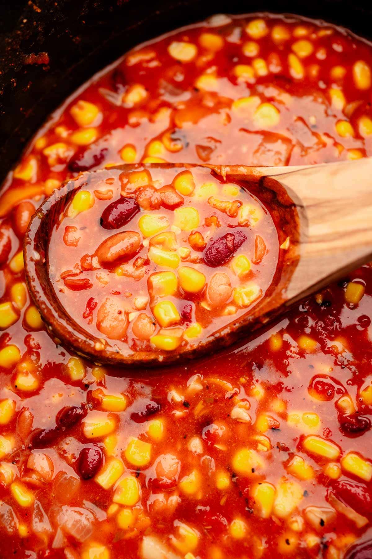 Slow cooker vegetarian chili is being stirred with a wooden spoon.