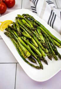 Grilled asparagus on a white plate with lemon wedges.